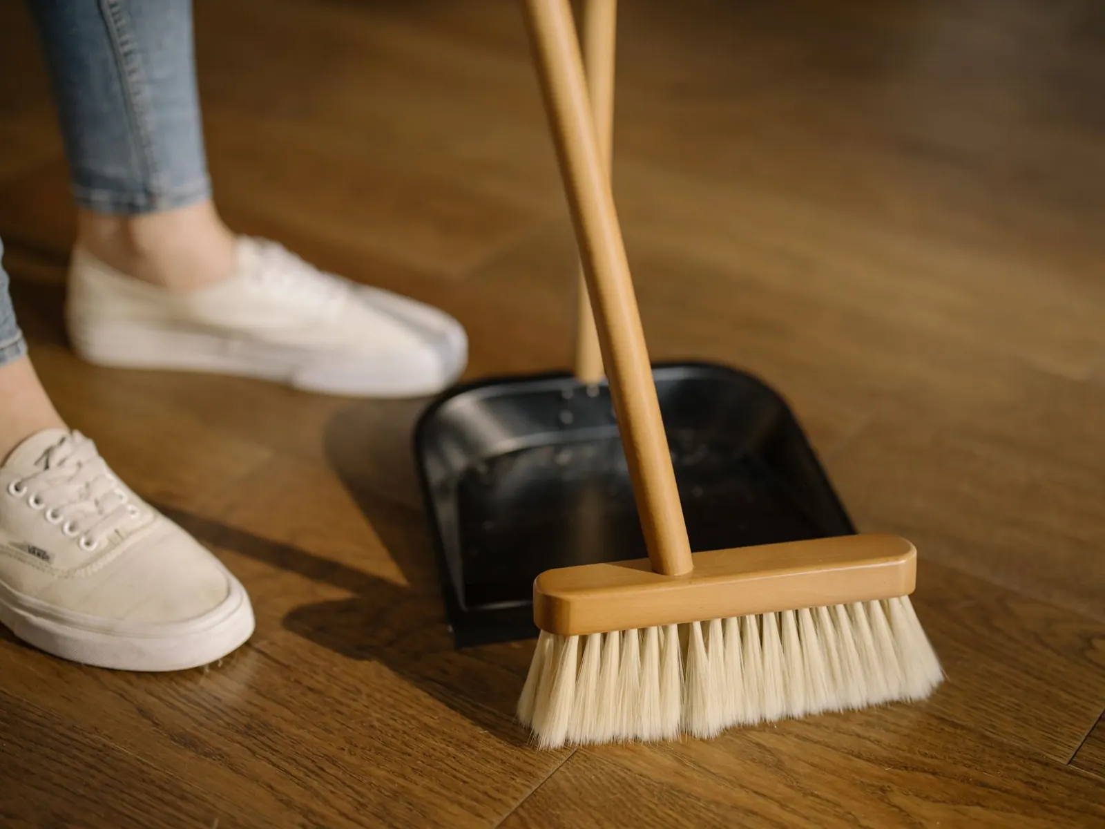 Close-up of a broom and dustpan sweeping a wooden floor