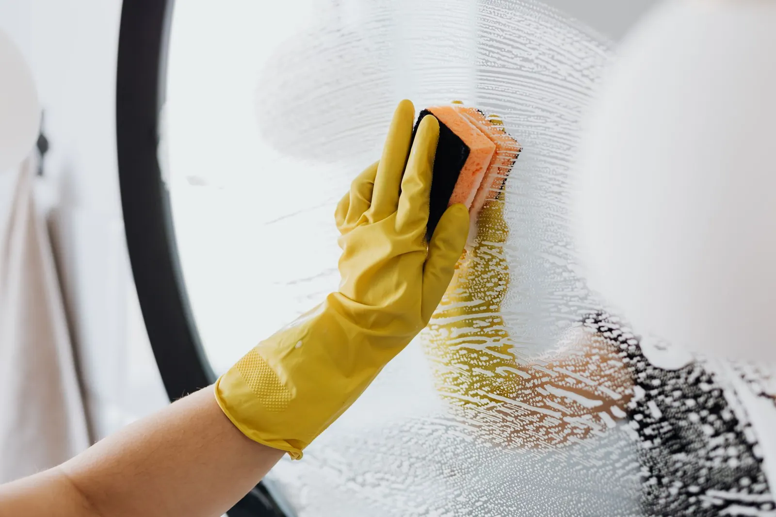 Cleaner in yellow gloves wiping a glass surface until it shines