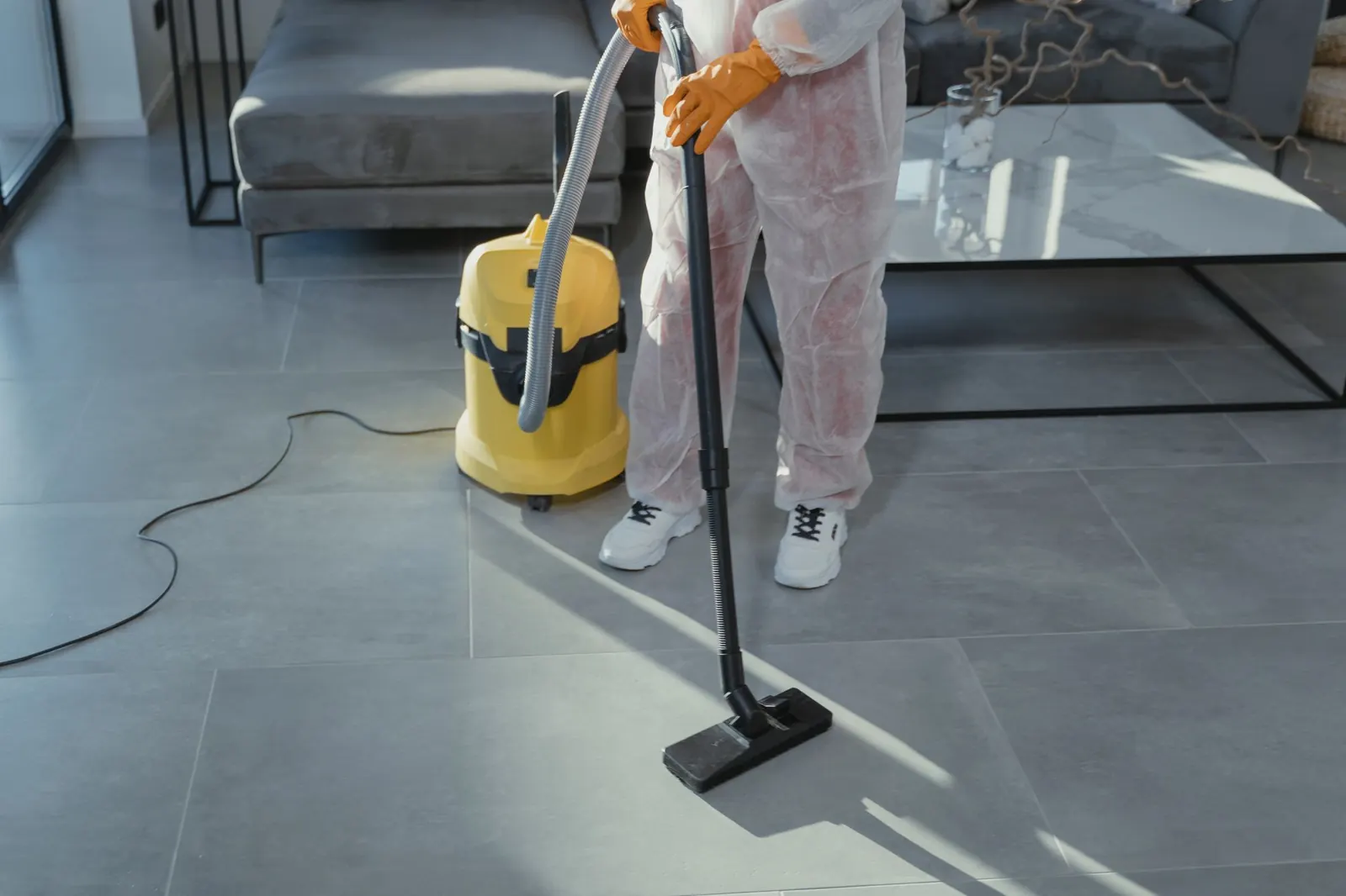 Cleaner vacuuming a bright living room floor with a yellow vacuum