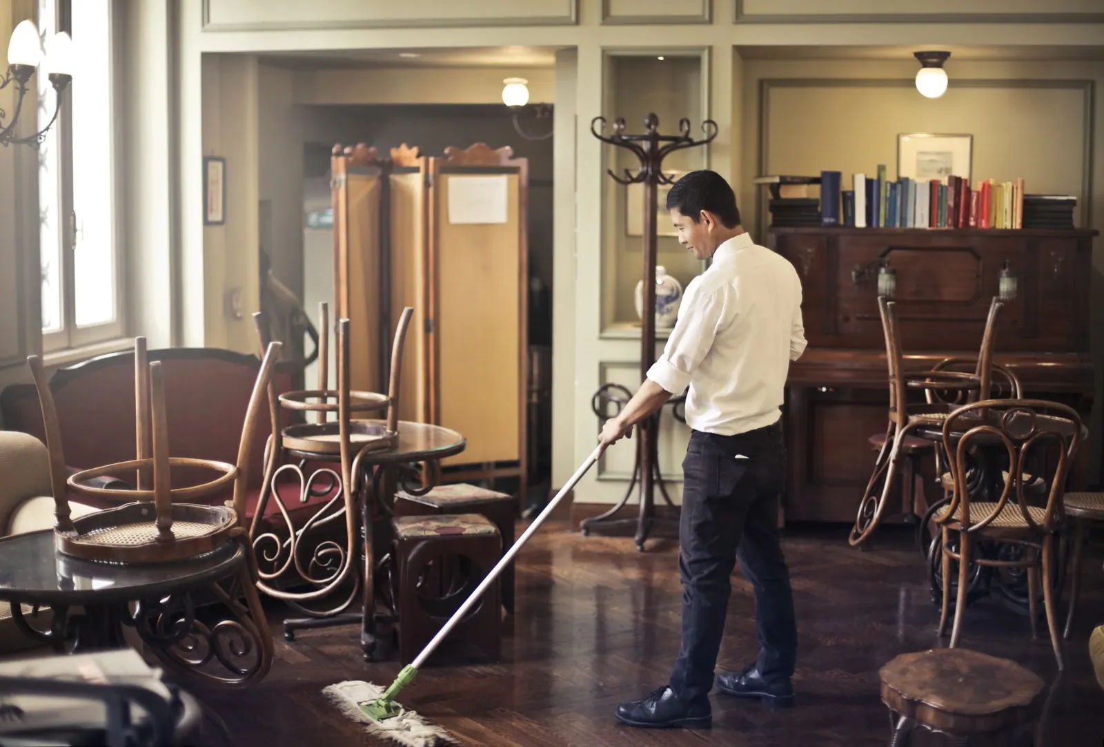 Cleaner mopping the floor of a restaurant dining room with chairs stacked on the tables